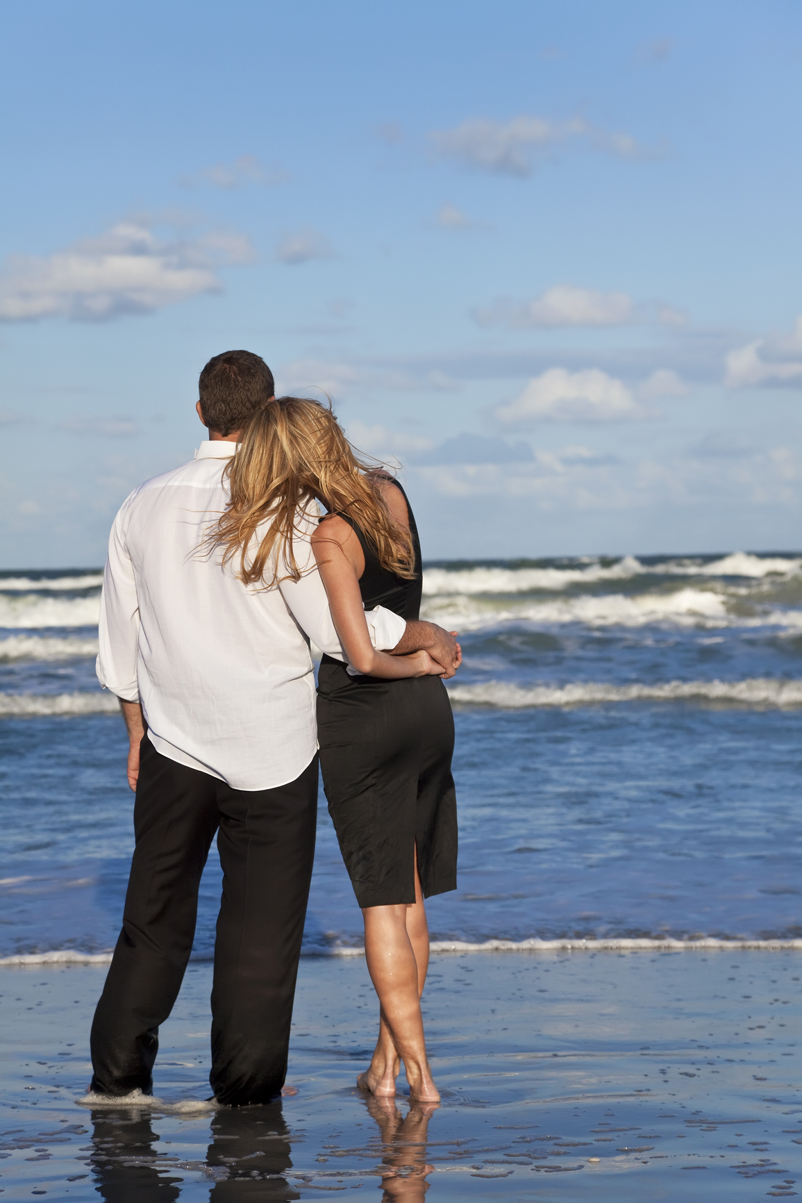 A young man and woman embracing as a romantic couple on a beach with a bright blue sky